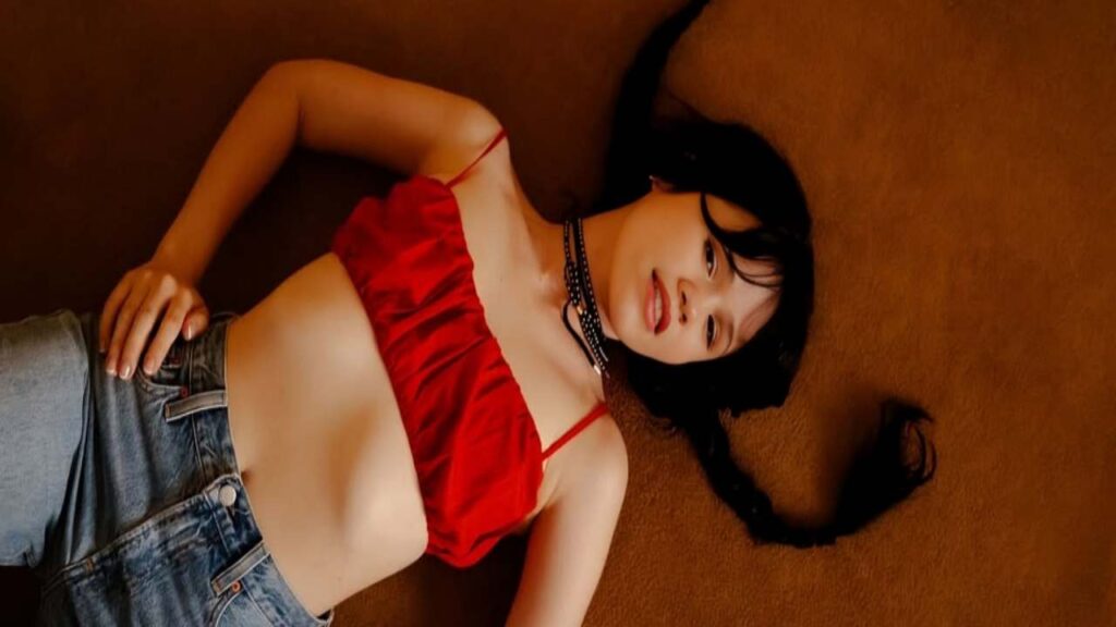 Yhivi in a red top is lying on the floor, appearing relaxed and contemplative.