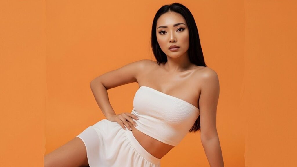 Ayumi Anime in a flowing white dress poses against a bold orange background, showcasing her style.

