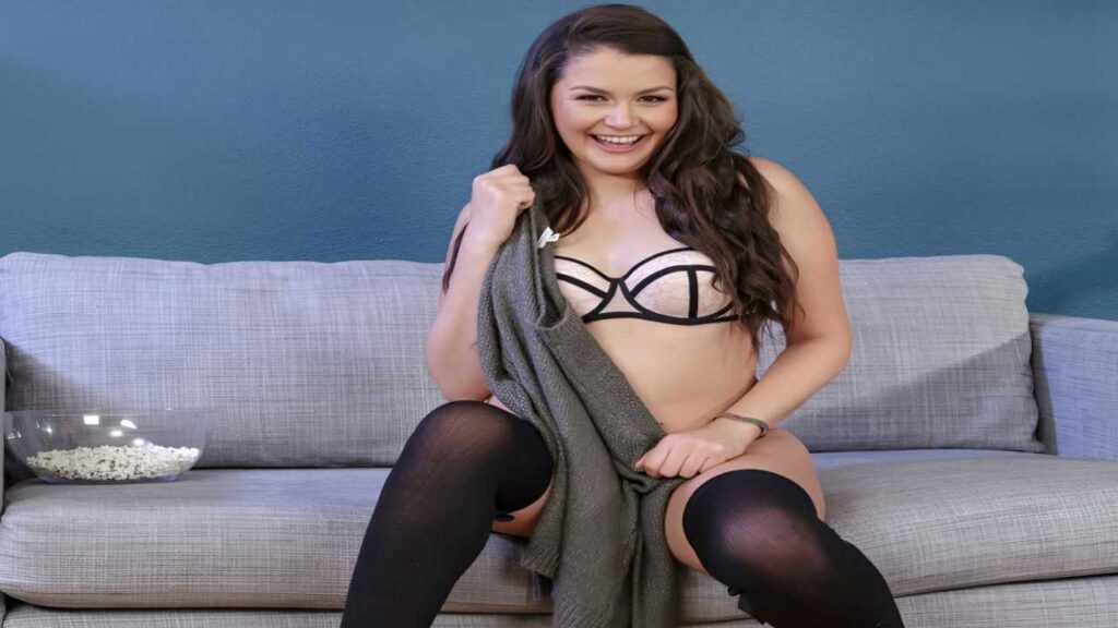 Allie Haze in a black bra and stockings sits elegantly on a couch, exuding confidence and style.
