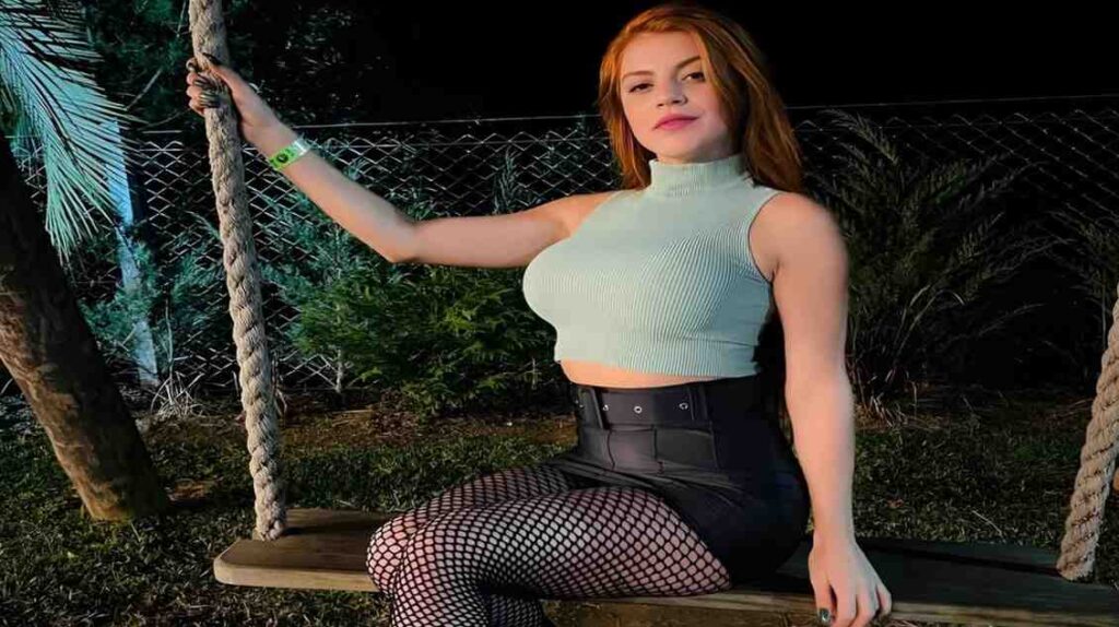 Anny Ward in fishnet stockings and a crop top sits on a swing, smiling and enjoying a sunny day outdoors
