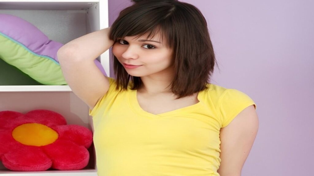 Ariel Rebel poses in front of a shelf filled with colorful toys, smiling and showcasing her playful surroundings