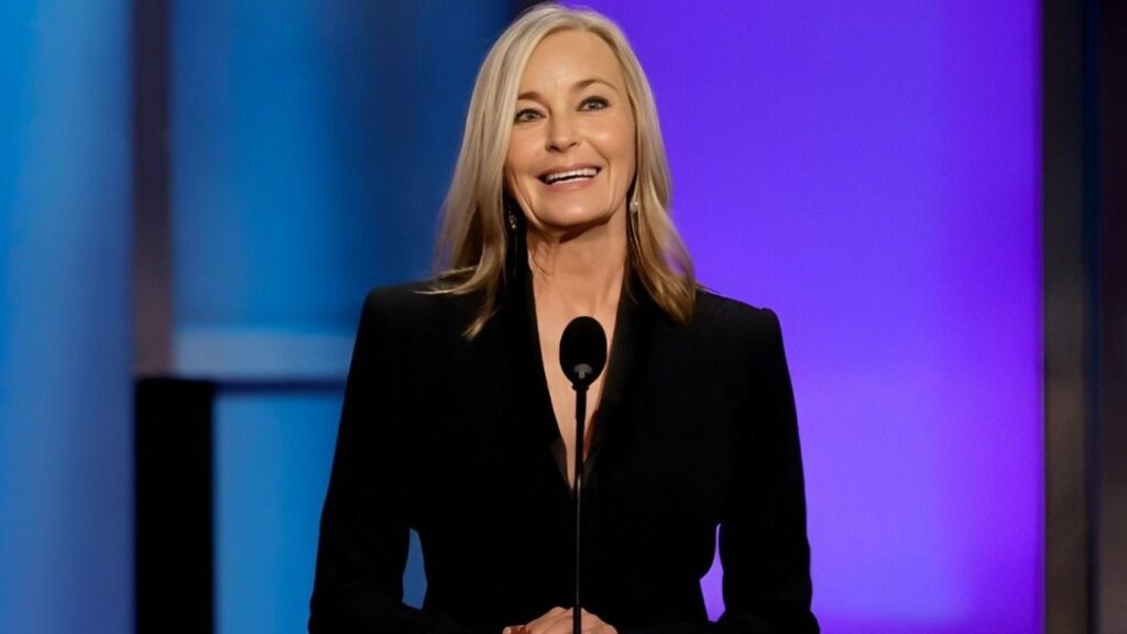 Bo Derek in a black suit stands confidently at a podium, preparing to address an audience