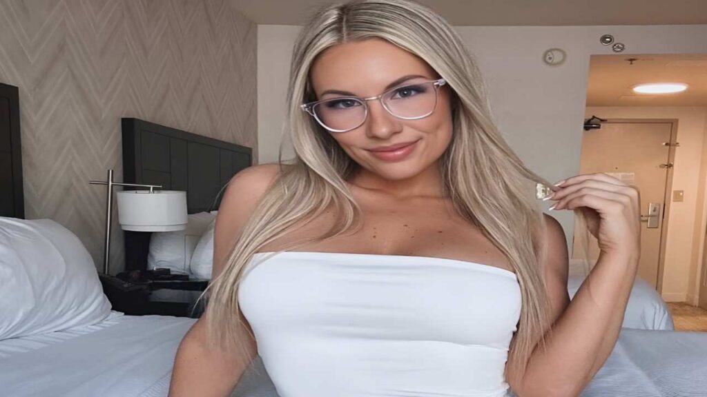 Bunny Madison in glasses wearing a white dress, standing confidently with a neutral background