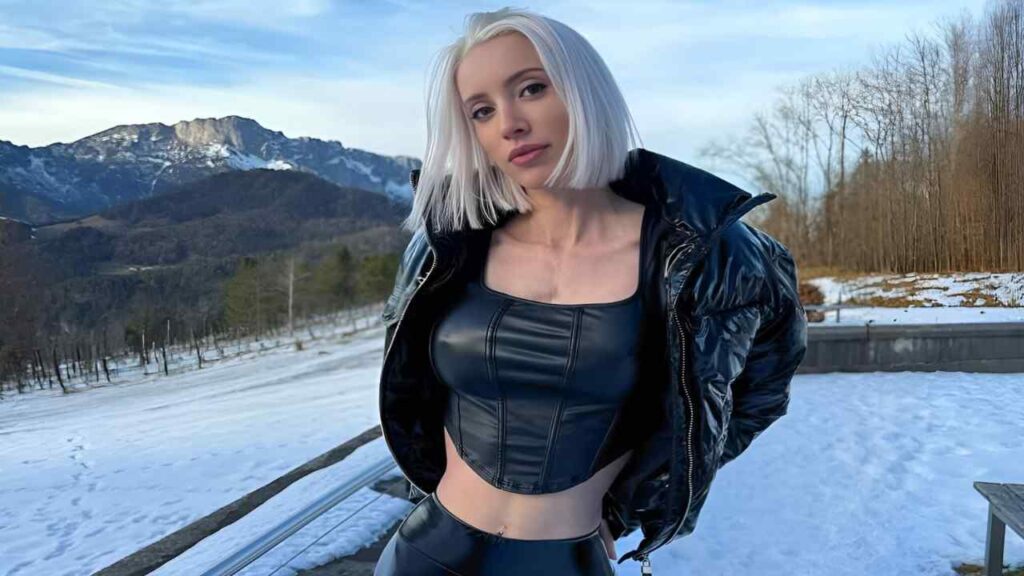 Candy XS in a black leather outfit poses confidently in a snowy landscape, showcasing her stylish look against the white backdrop