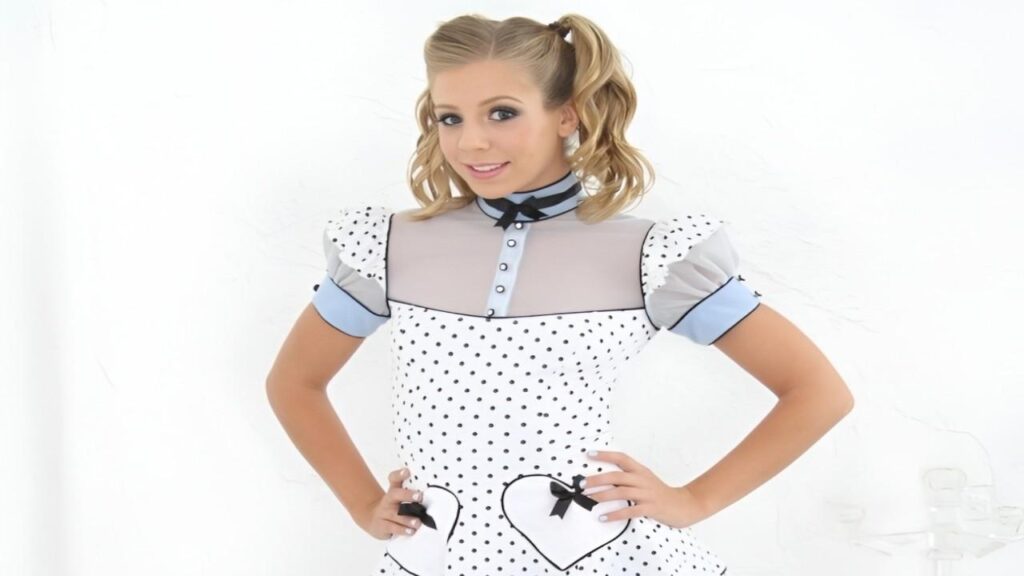 Chastity Lynn in a polka dot dress poses for a picture, smiling and standing confidently against a neutral background