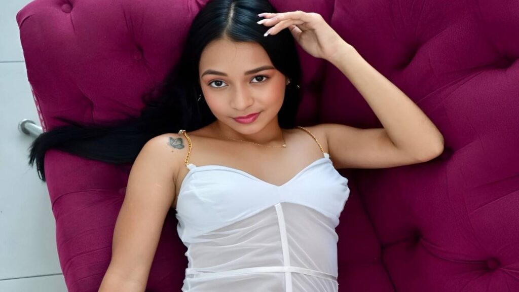 Emma Anturin in a white top and panties reclines on a purple couch, creating a relaxed and casual atmosphere.