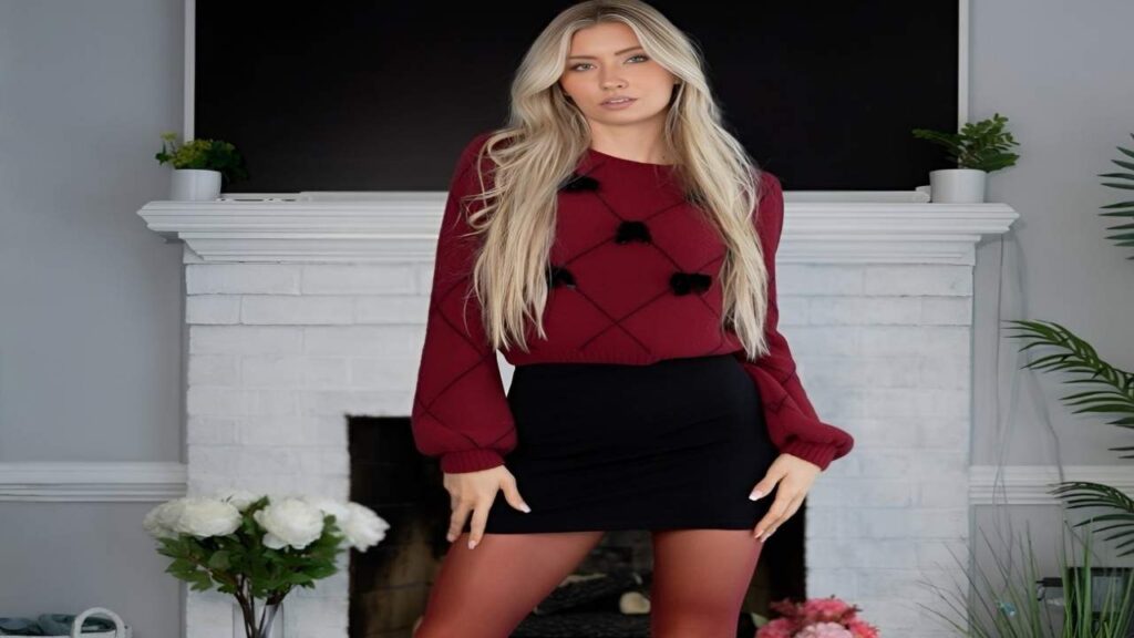 Emma Sirus in a red sweater and black skirt poses confidently for the camera, smiling warmly.