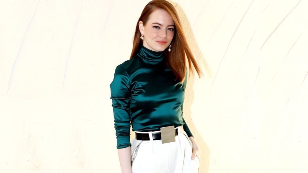 Emma Stone wearing a green turtleneck and white pants stands confidently, showcasing a stylish and modern outfit