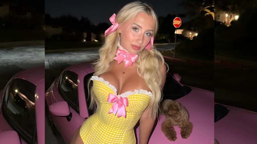 Grace Morris woman in a yellow gingham dress stands beside a pink car, smiling in a sunny outdoor setting