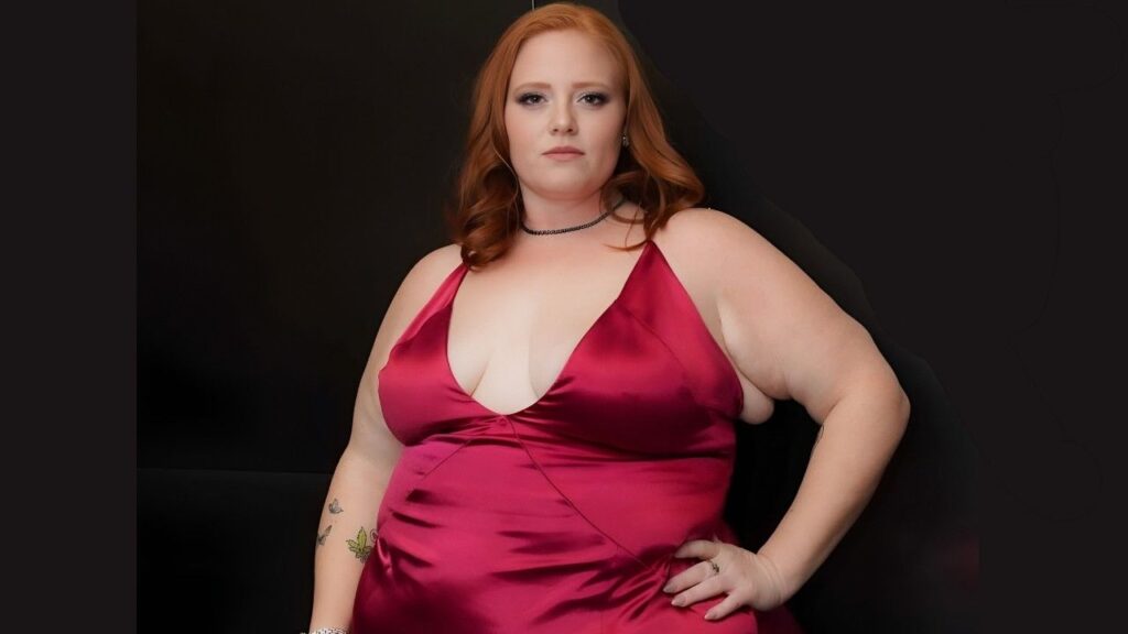 Julie Ginger in a red dress poses confidently for a photo, smiling at the camera.
