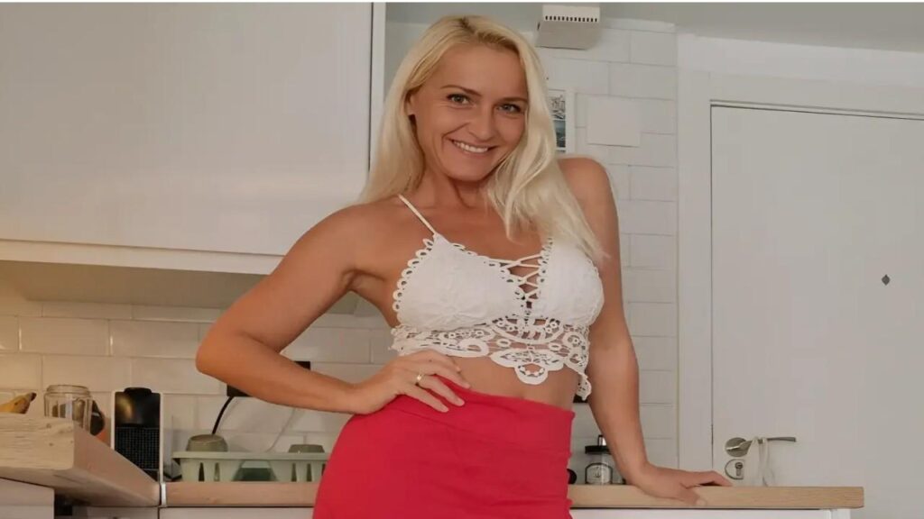 Kathia Nobili wearing a red skirt and a white top stands confidently, smiling at the camera.