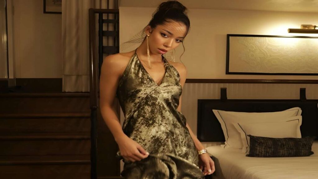 Lia Lin in a green dress stands elegantly in a well-decorated hotel room