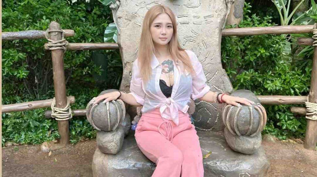 Meng Ruoyu sits atop a large statue in a park, surrounded by greenery and enjoying the outdoor scenery