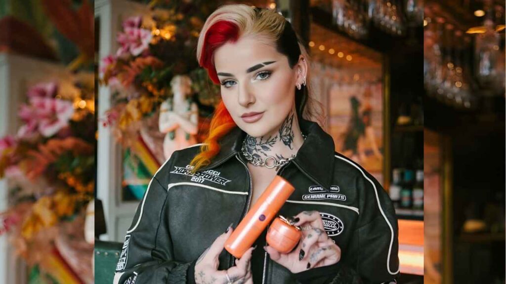 Molly Hull with tattoos sits on a large chain, showcasing her body art against an industrial backdrop