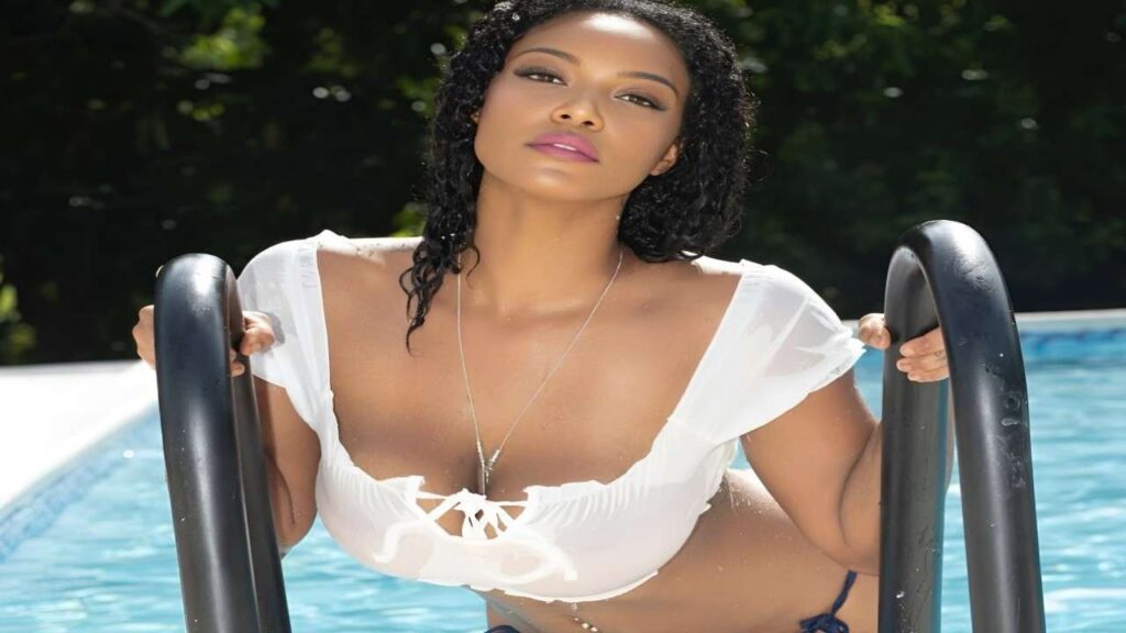 Montana Fishburne in a bikini poses confidently by a sparkling blue pool under a clear sky.