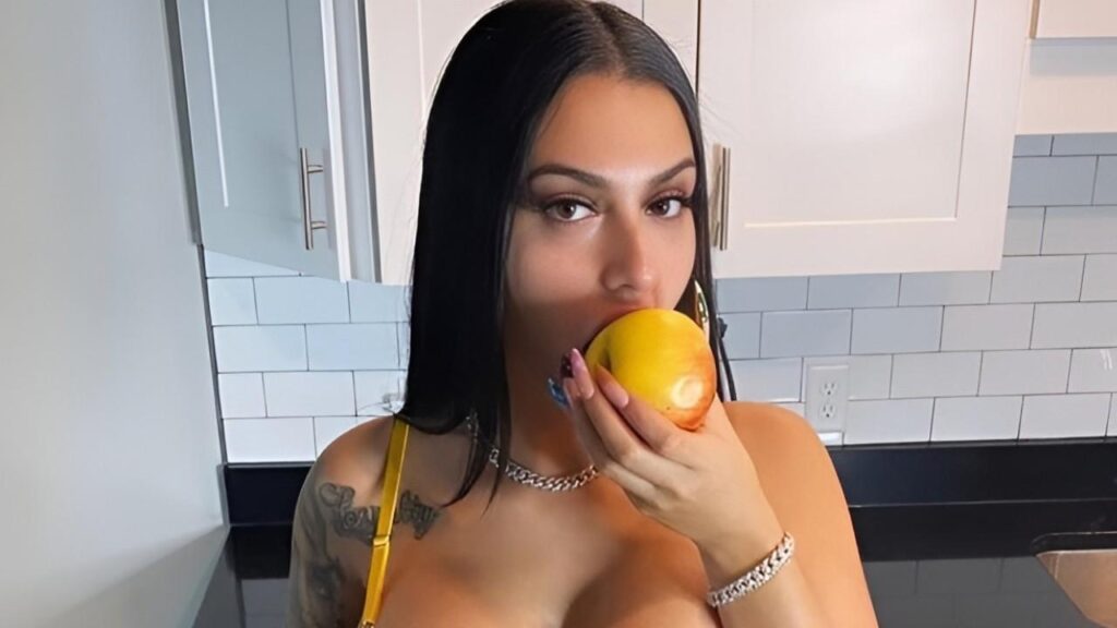 Nadia Goher with tattoos enjoys eating a juicy orange, showcasing her vibrant body art and a moment of refreshment.