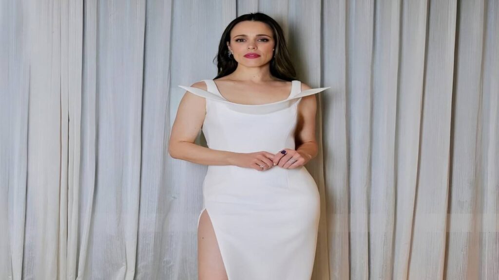 Rachel McAdams in a white dress poses confidently for the camera, smiling and looking directly at the viewer