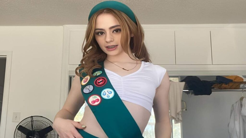 Reese Robbins wearing a green sash and a badge on her chest, standing confidently with a neutral expression.
