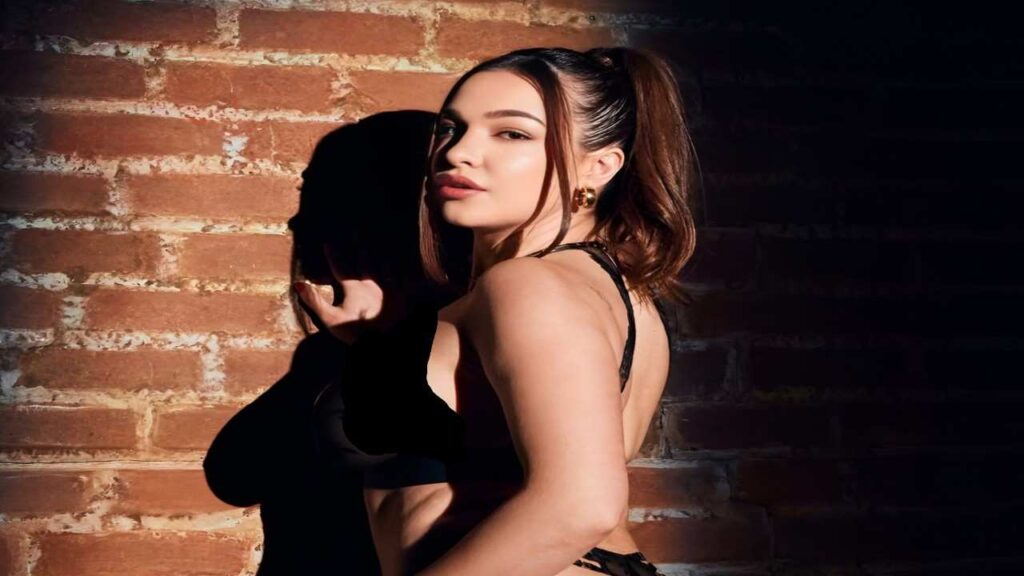 Rissa May wearing a black bra top and matching black panties poses confidently.