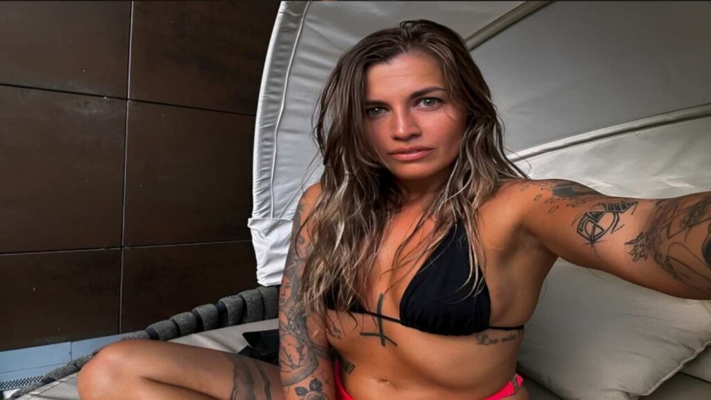 Silvia Dellai with tattoos sits comfortably on a chair, showcasing her body art and relaxed demeanor