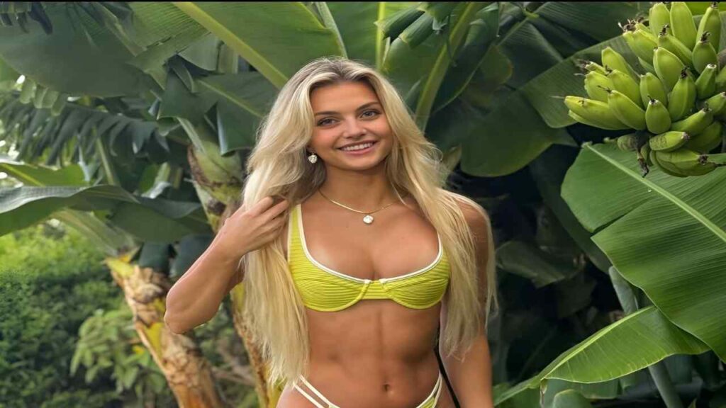 Trippie Bri  in a yellow bikini stands beside a bunch of ripe bananas on a sunny day.