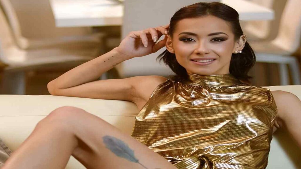 Veronica Leal in a gold dress sits elegantly on a couch, exuding a sense of style and sophistication.