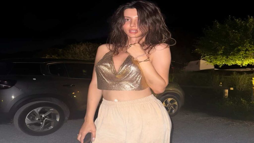 Vicats in a gold top and skirt poses confidently for a photograph, showcasing her stylish outfit.