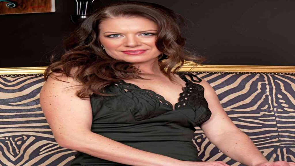 Amanda Blake in a black dress sits elegantly on a zebra print couch, showcasing a stylish and modern interior setting