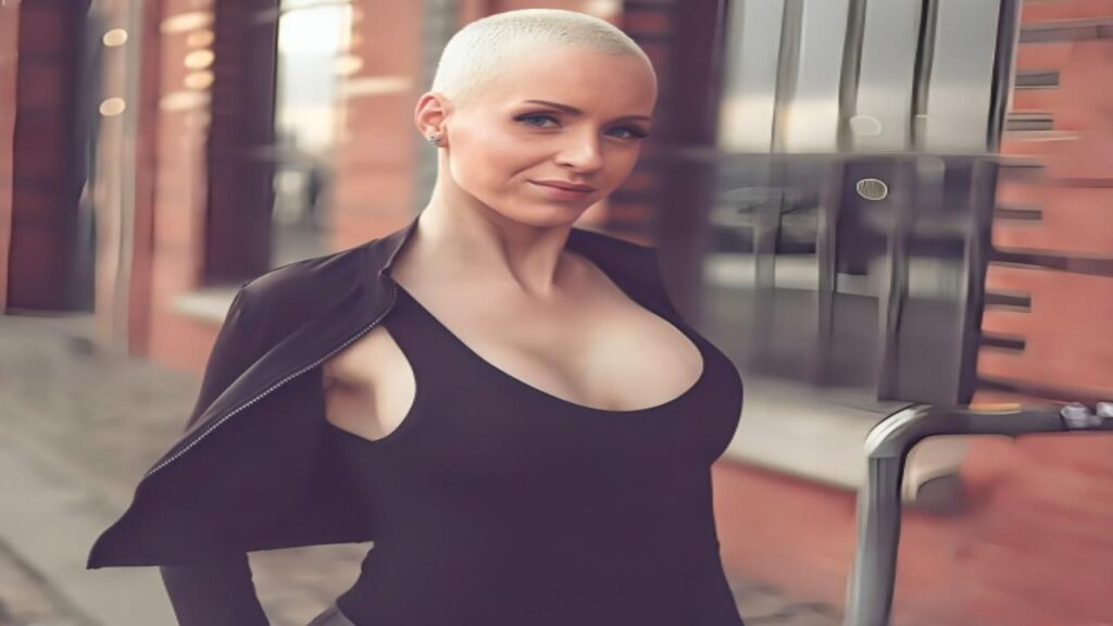 Anike Ekina with a shaved head wearing a black top, looking confidently at the camera.