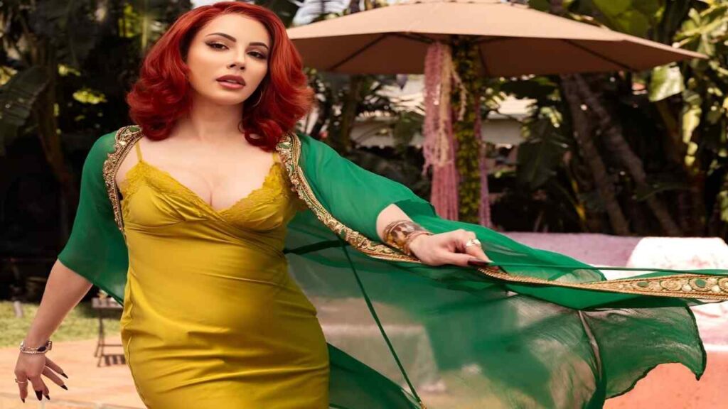 Ariel Demure wearing a green dress and a gold shawl stands elegantly, showcasing her stylish outfit