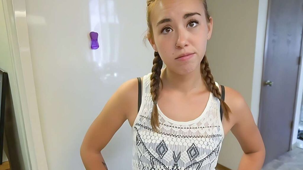 Brandi Braids with braids stands in front of an open refrigerator, looking inside with curiosity.