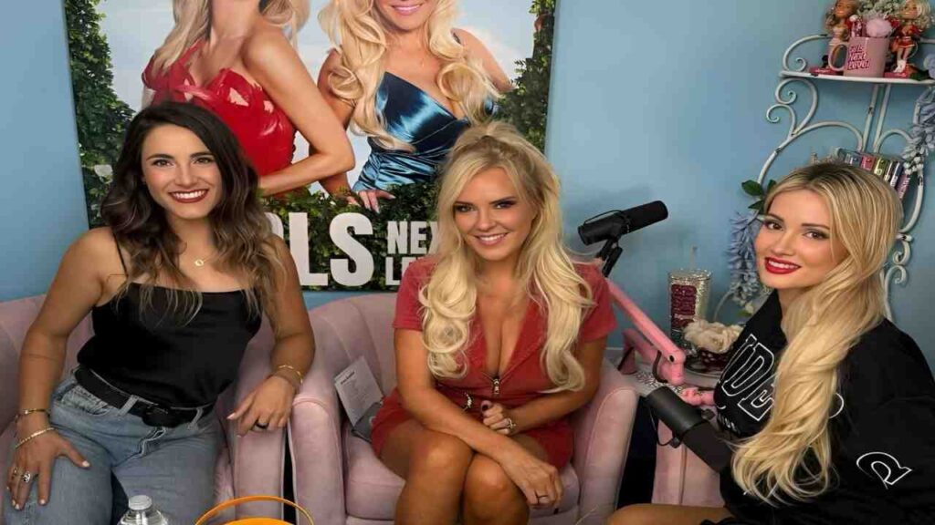 Bridget Marquardt sit on a couch, smiling, with a colorful poster hanging on the wall behind them.