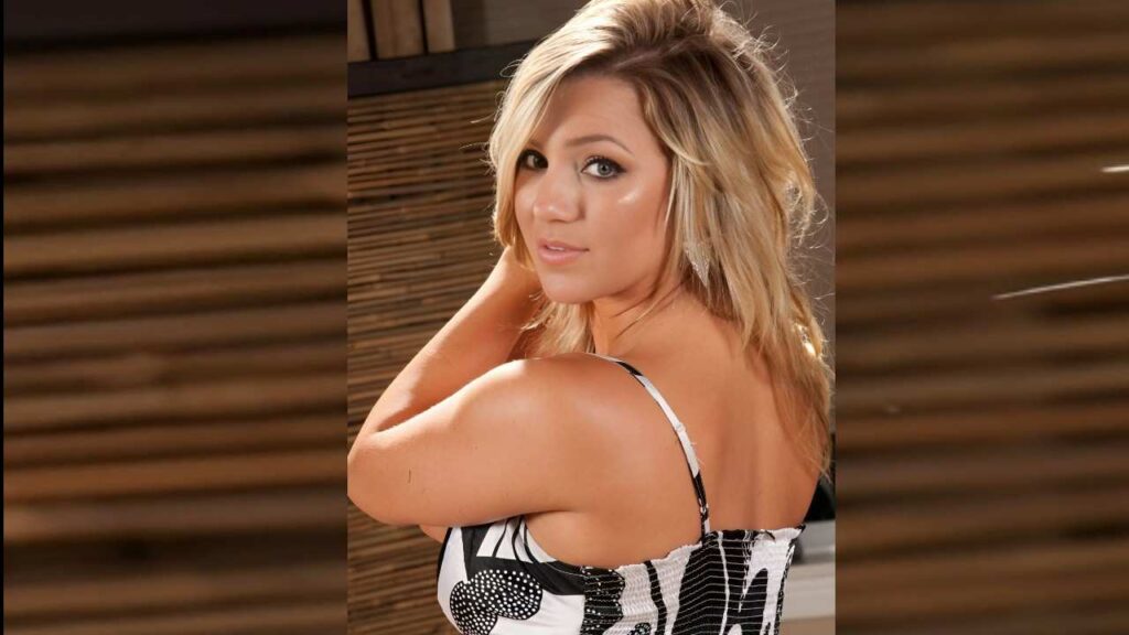 Cameron Dee poses for a photo, wearing a stylish black and white dress, with a confident expression.