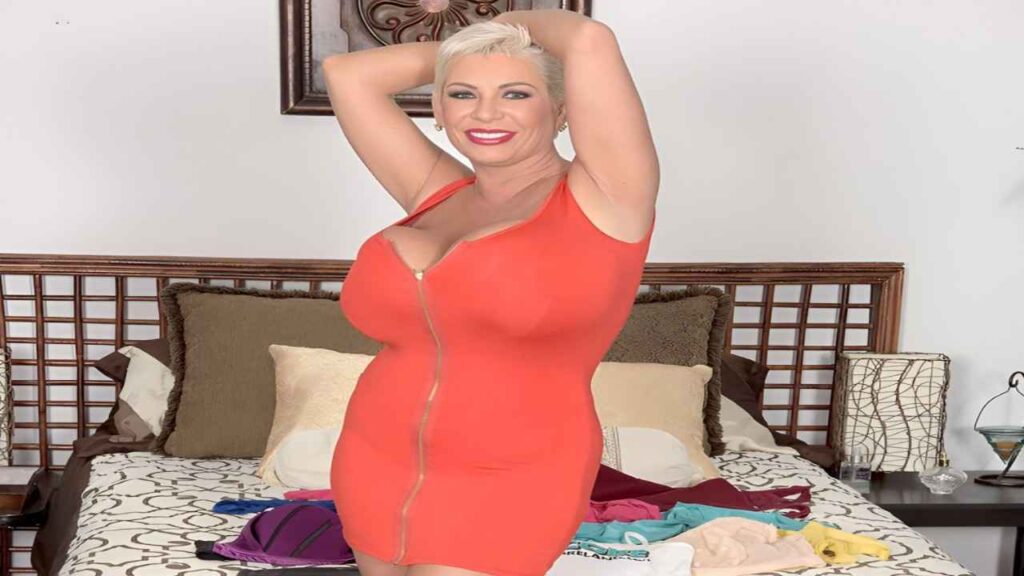 Claudia Marie in a red dress poses gracefully on a bed, showcasing elegance and style in a cozy setting