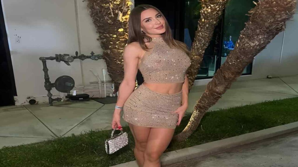 Ella Reese in a shimmering gold dress poses elegantly for a photograph, showcasing her confident demeanor.