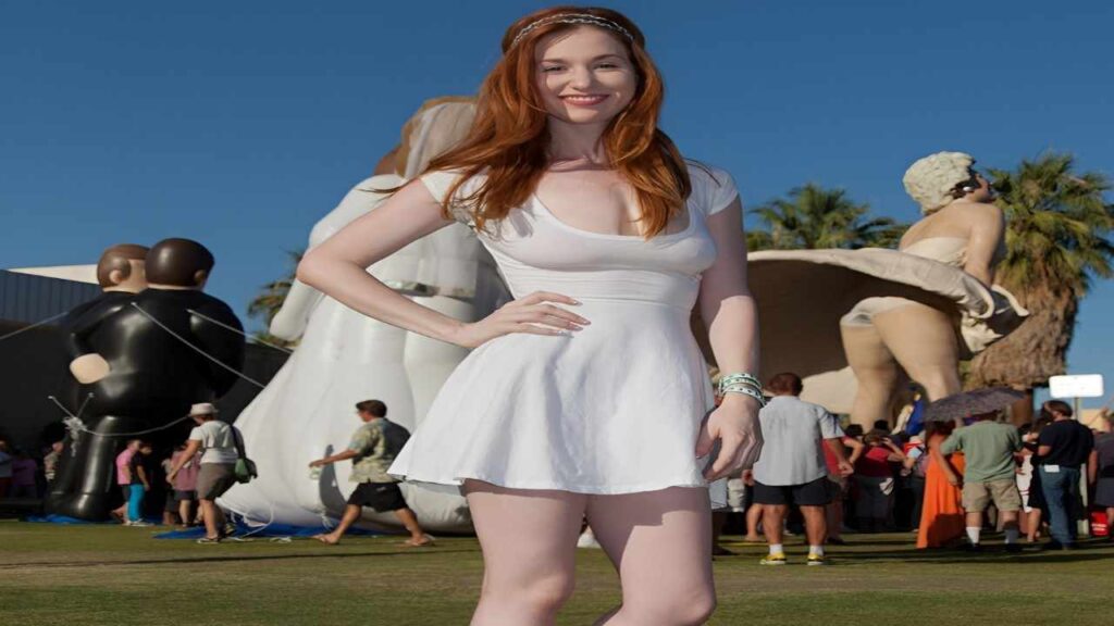 Emily Archer in a white dress poses confidently in front of a large, colorful inflatable structure.