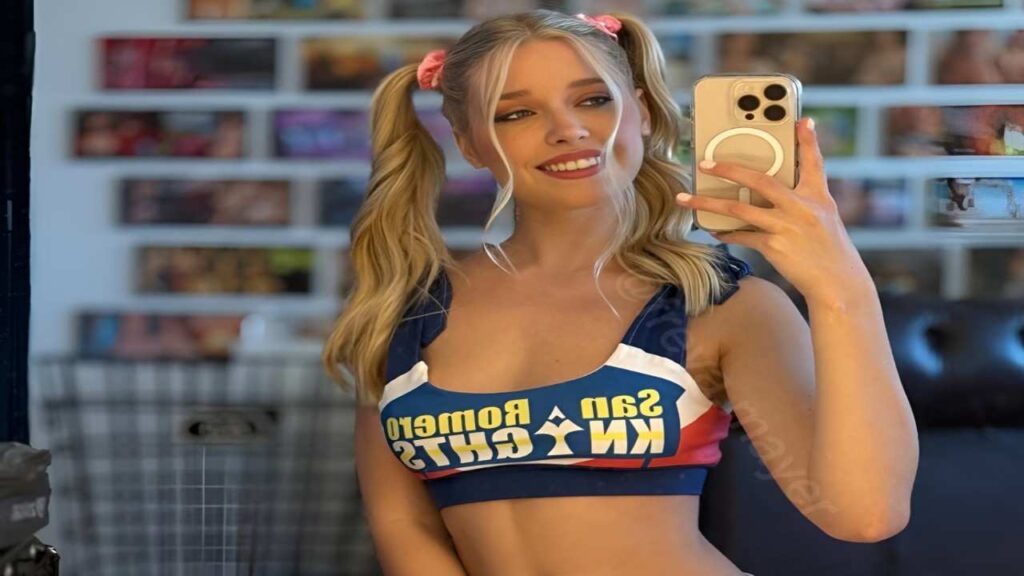 Freya Mayer in a cheerleader outfit smiles while taking a selfie with her phone