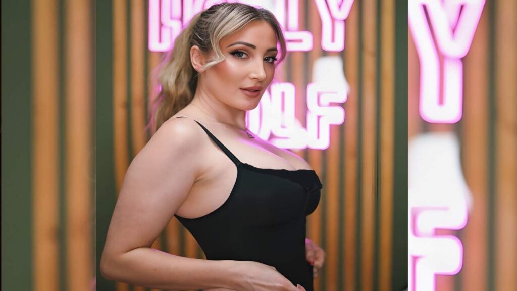 Holly Wolf in a black bodysuit poses confidently in front of a vibrant neon sign, showcasing a modern urban aesthetic