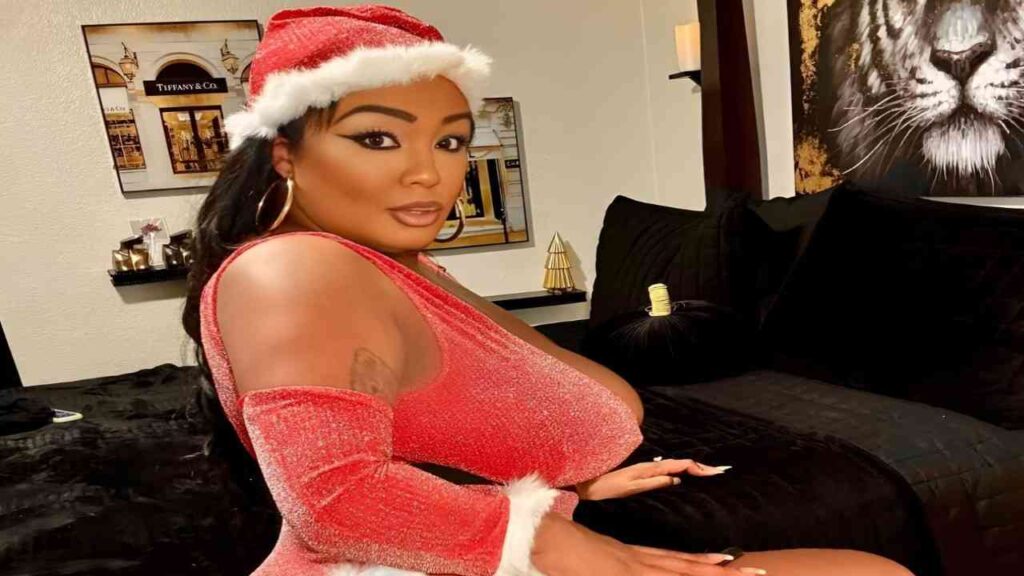 Layton Benton wearing a Santa hat sits on a bed, smiling and enjoying a festive atmosphere.