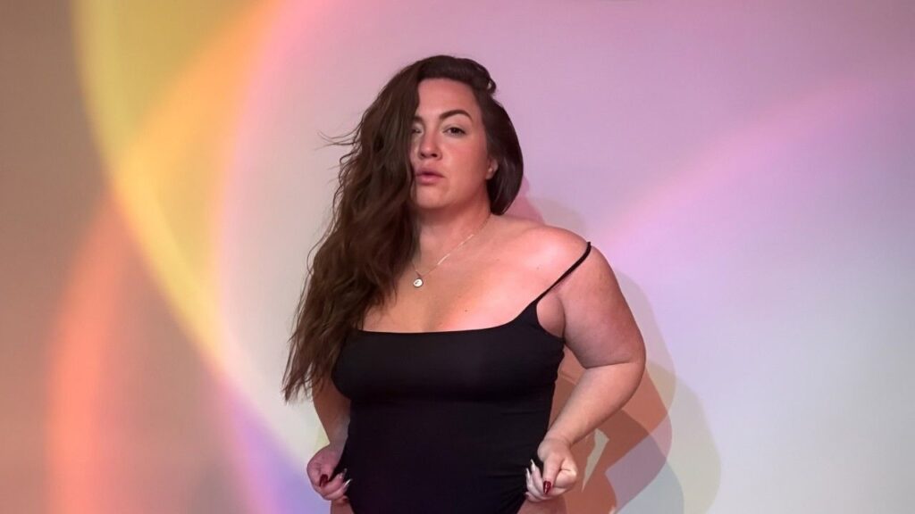 Maddy Oreilly in a black bodysuit poses confidently against a vibrant, colorful background.