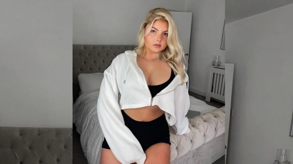 Milly Morris wearing a white hoodie and black shorts stands casually, showcasing a relaxed and sporty outfit