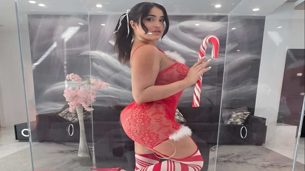 Nia Bleu in red stockings holds a large candy cane, smiling cheerfully against a festive background