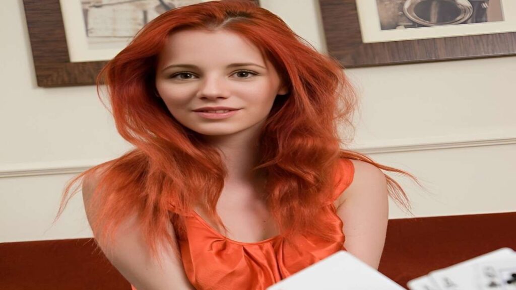 Piper Fawn with vibrant red hair holds a deck of cards, smiling confidently at the camera.