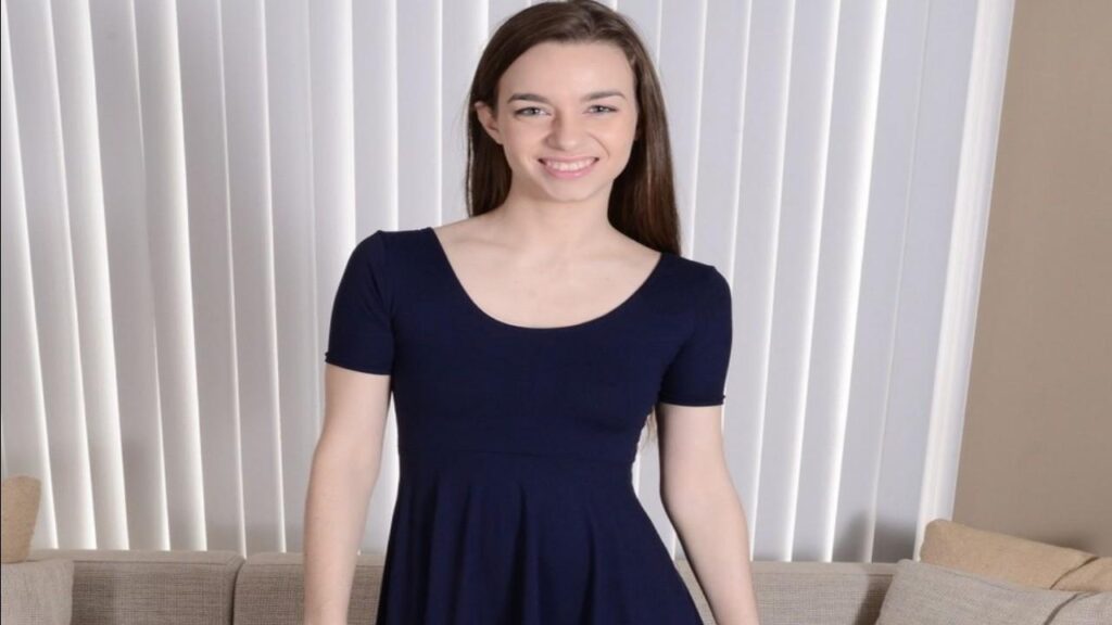 Tali Dova in a blue dress poses confidently for the camera, smiling and looking directly at the viewer