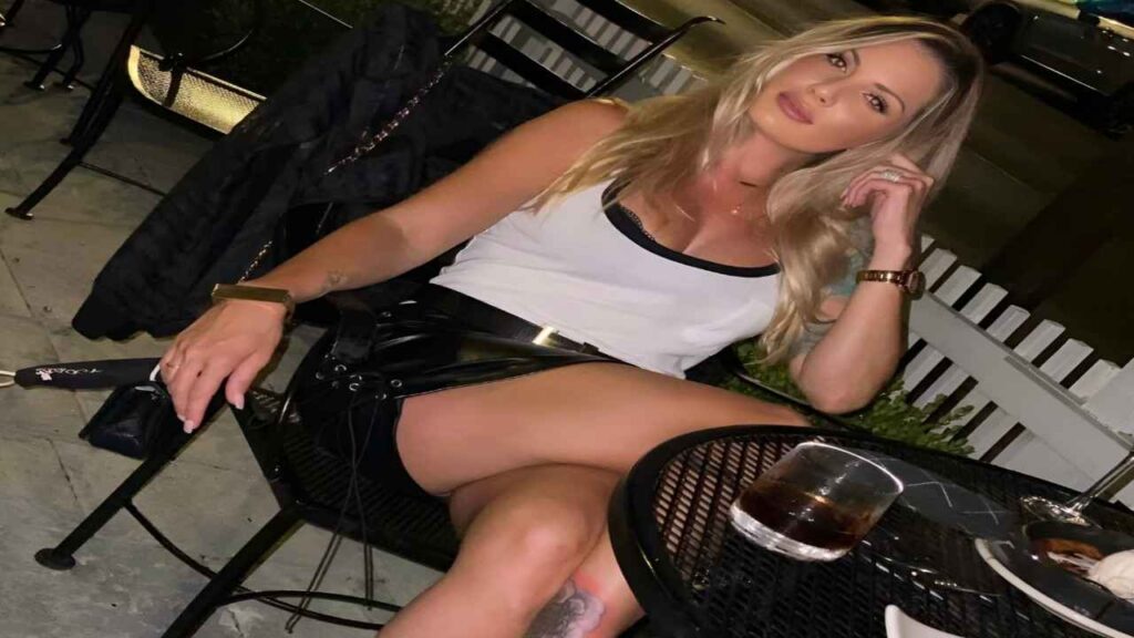 Teagan Presley sits at a table, holding a cigarette in one hand and a drink in the other, appearing contemplative