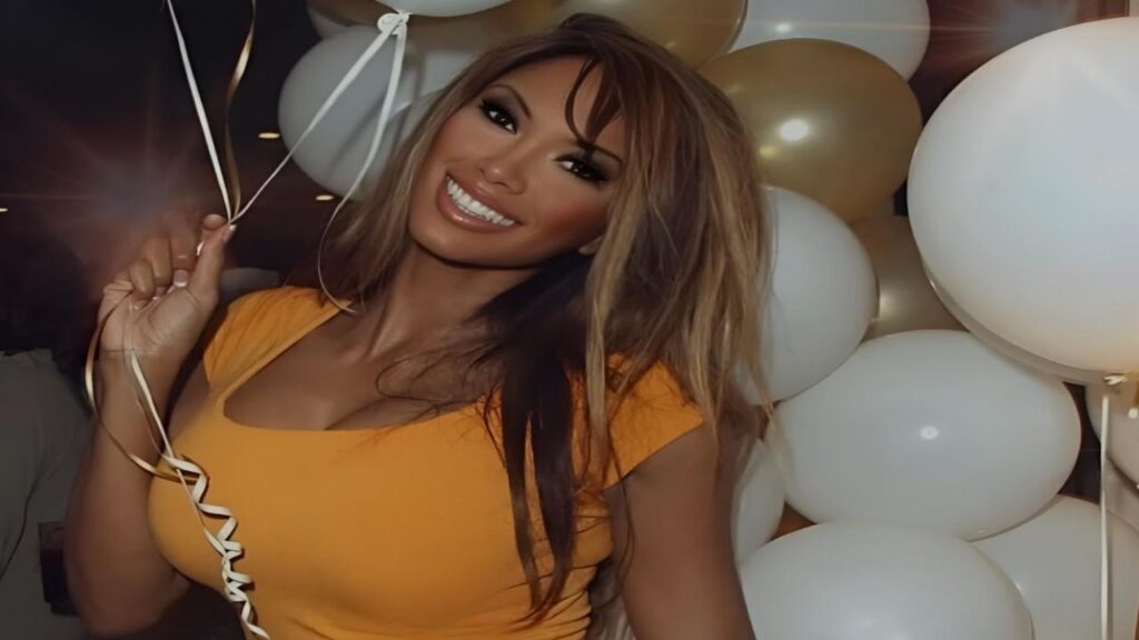 Traci Bingham in a yellow top joyfully holds a cluster of colorful balloons against a bright background
