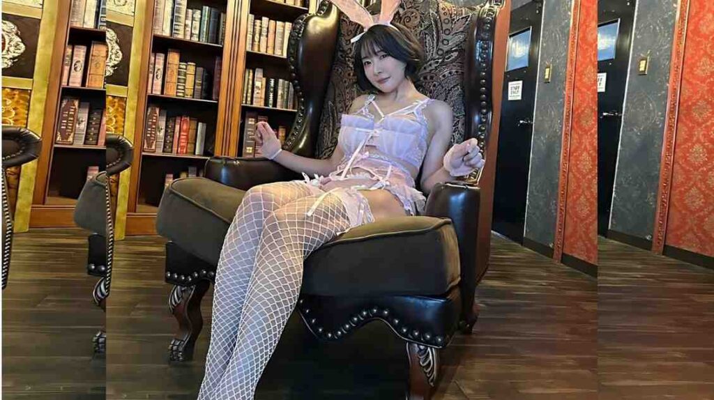 Arisa Hanyu in lavender and fishnet stockings lounges in an ornate leather chair with bunny ears, in a cozy library