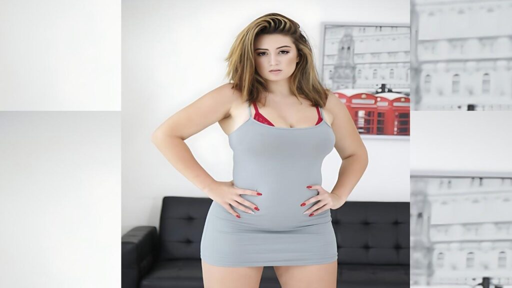 Britt James with shoulder-length blonde hair in a light gray bodycon dress, hands on hips in a bright living room.