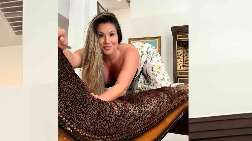 Coco Vandi with long blonde hair in a floral white top leans over a leopard-print chaise, smiling in a bright, elegant room.