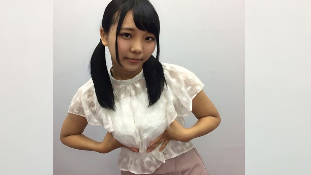 Ruka Inaba with twin pigtails in a lace white blouse and pale pink skirt, smiling softly.
